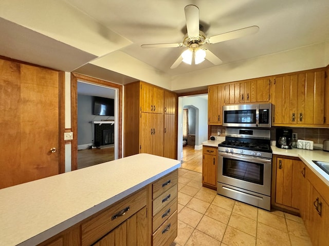 kitchen with a brick fireplace, ceiling fan, stainless steel appliances, and tasteful backsplash