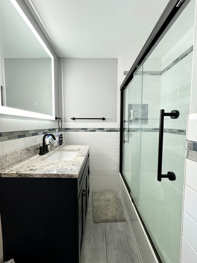 bathroom with vanity, combined bath / shower with glass door, and tile walls