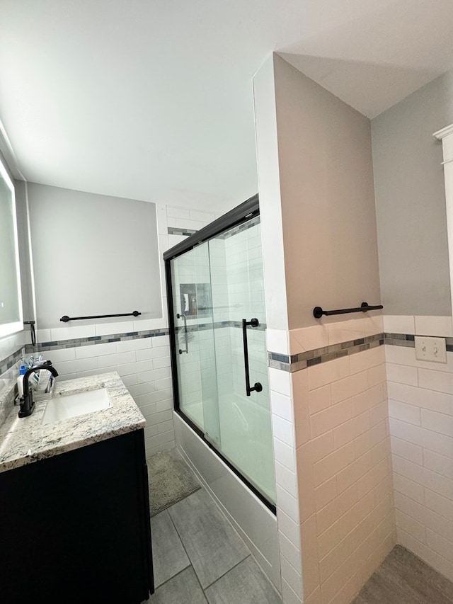 bathroom with tile patterned floors, shower / bath combination with glass door, vanity, and tile walls