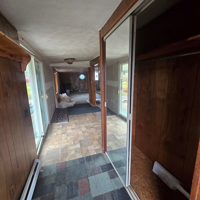 hallway featuring wooden walls, plenty of natural light, and a baseboard radiator