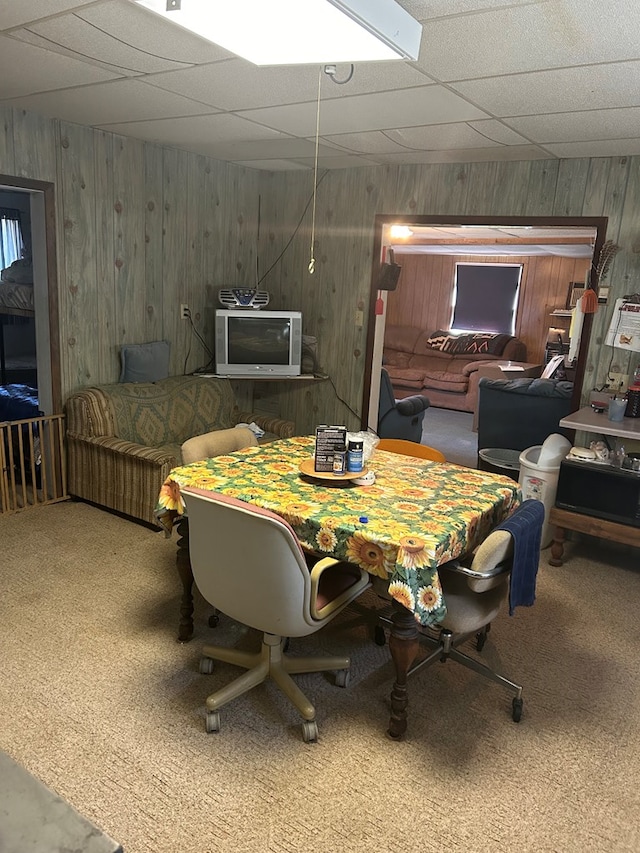 carpeted dining area with a paneled ceiling and wood walls