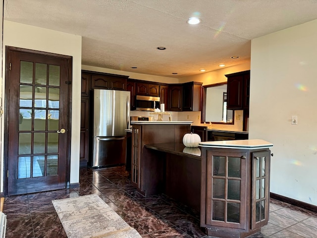 kitchen featuring appliances with stainless steel finishes, a center island, kitchen peninsula, dark brown cabinets, and a textured ceiling