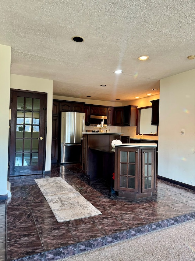 kitchen with a kitchen island, appliances with stainless steel finishes, a textured ceiling, and dark brown cabinetry