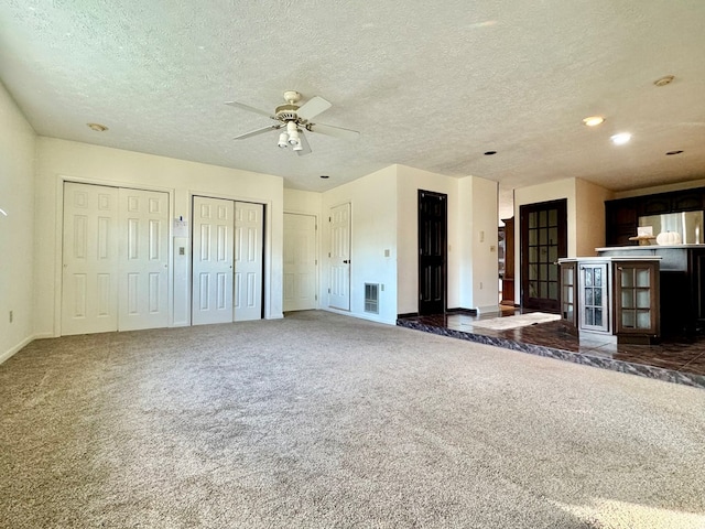 unfurnished living room with ceiling fan, a textured ceiling, and dark carpet