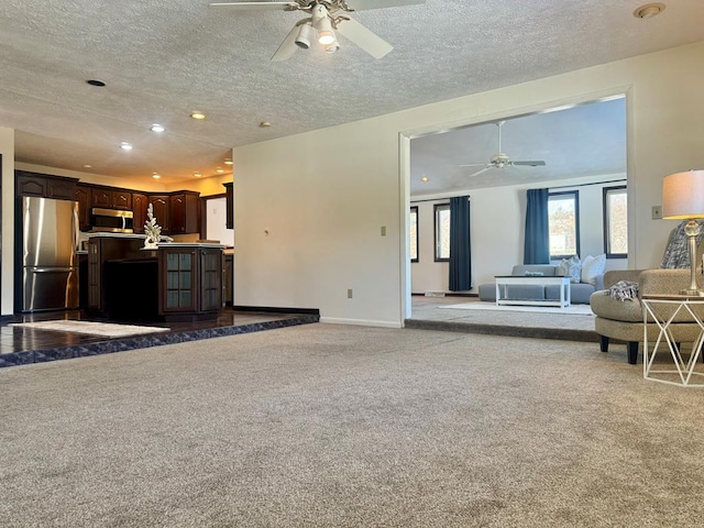 unfurnished living room featuring ceiling fan, light colored carpet, and a textured ceiling