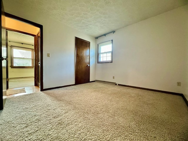 unfurnished bedroom featuring light colored carpet, a closet, a textured ceiling, and baseboard heating