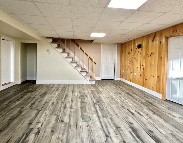 basement featuring hardwood / wood-style floors, a drop ceiling, and wood walls