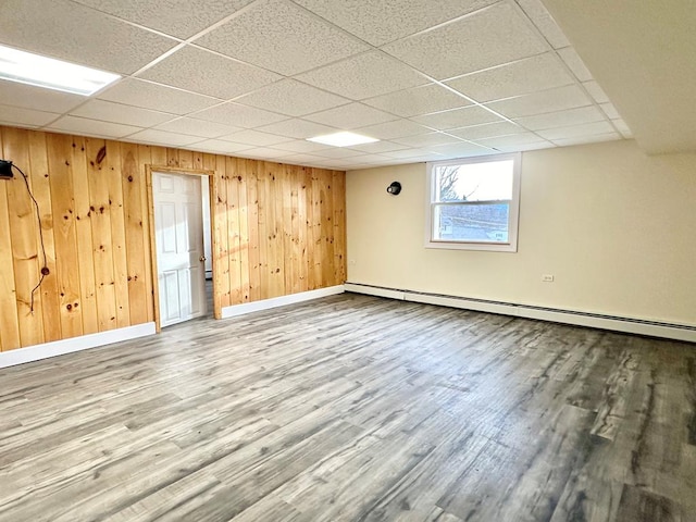 basement with wood-type flooring, wooden walls, a drop ceiling, and baseboard heating