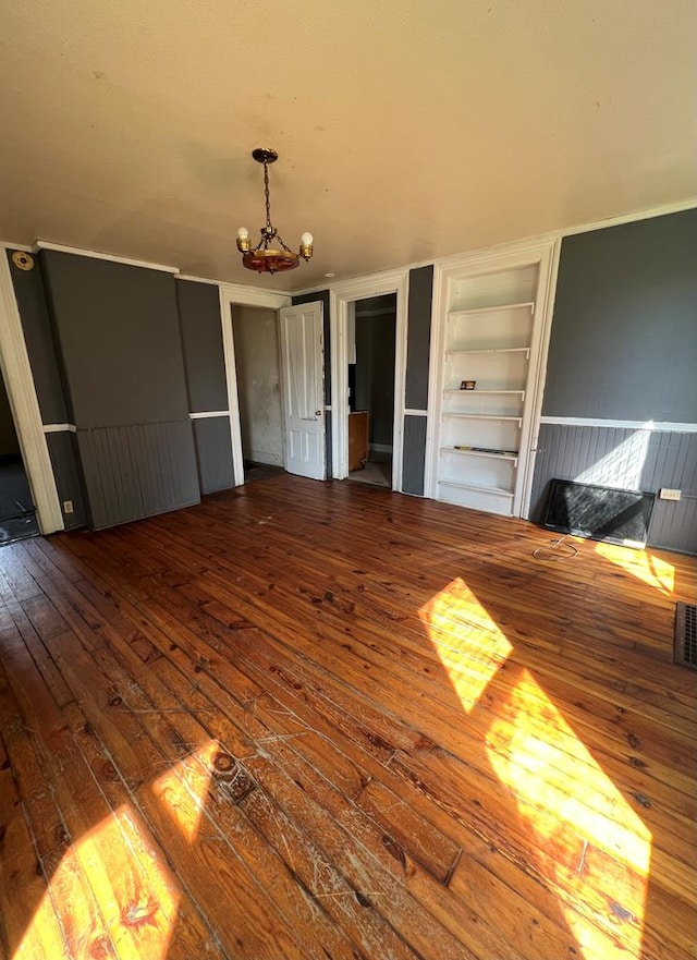 unfurnished living room with wood-type flooring, built in features, and a chandelier