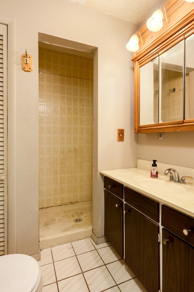 bathroom featuring tile patterned floors, a textured ceiling, vanity, tiled shower, and toilet