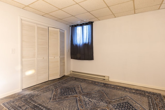 unfurnished bedroom featuring a paneled ceiling, a baseboard radiator, and a closet