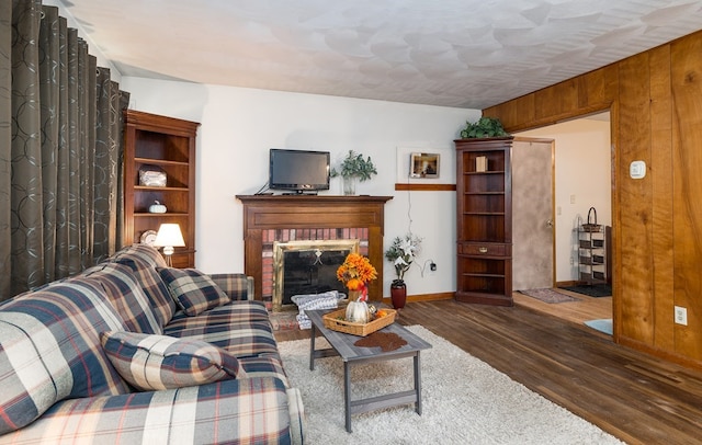 living room with dark hardwood / wood-style floors, wood walls, and a brick fireplace