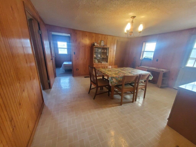 dining room featuring a chandelier, a textured ceiling, a wealth of natural light, and wood walls