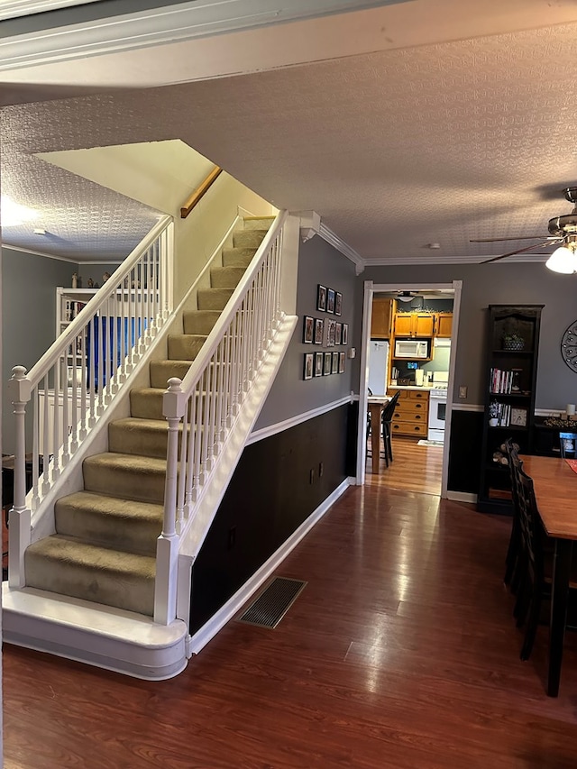 staircase featuring ceiling fan, ornamental molding, a textured ceiling, and hardwood / wood-style flooring