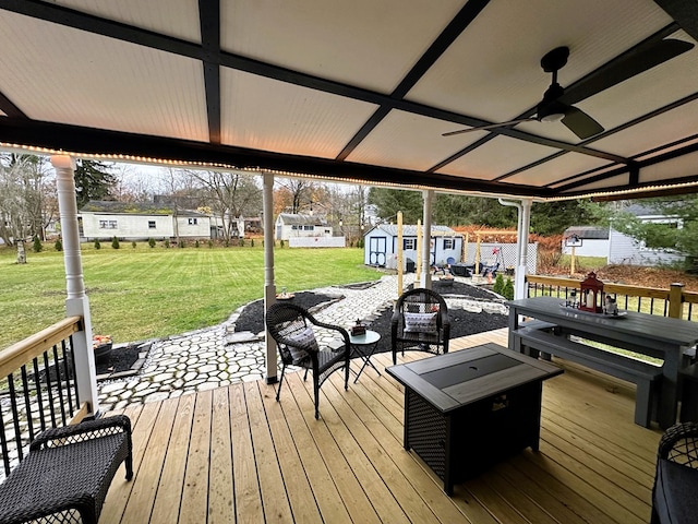 deck with an outdoor fire pit, ceiling fan, a storage shed, and a lawn