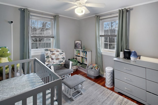 bedroom featuring a crib, a ceiling fan, ornamental molding, and dark wood-type flooring