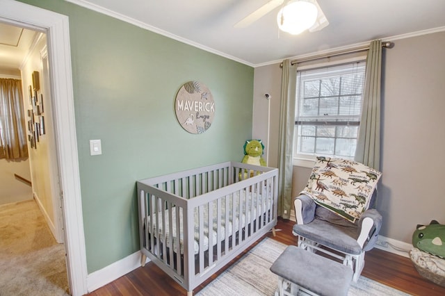 bedroom featuring crown molding, a crib, wood finished floors, and baseboards