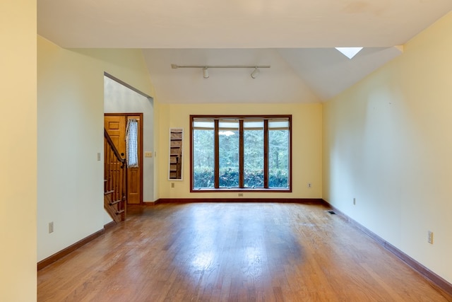 spare room featuring rail lighting, light hardwood / wood-style flooring, and vaulted ceiling with skylight