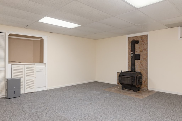 basement featuring carpet, a wood stove, and a drop ceiling