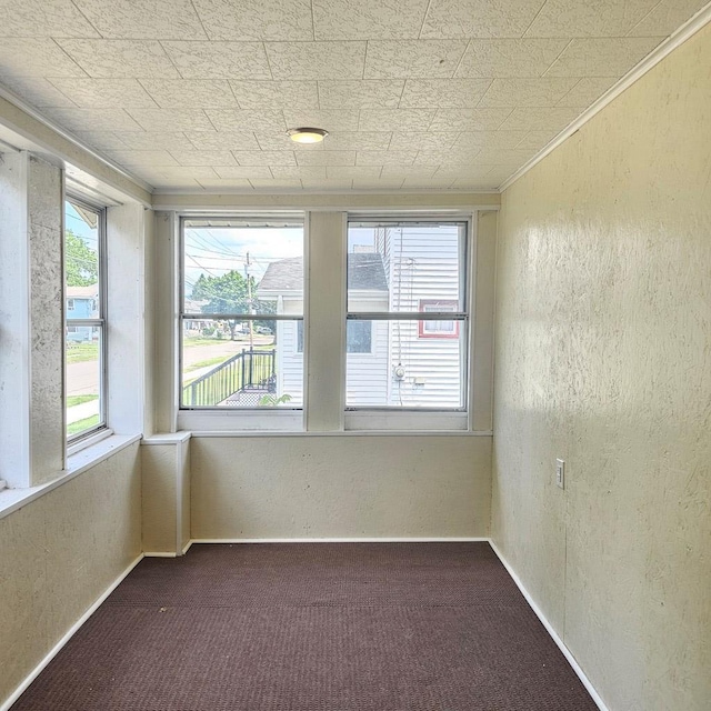 spare room with plenty of natural light, ornamental molding, and dark colored carpet