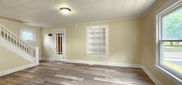 unfurnished room with wood-type flooring, ornamental molding, and built in shelves