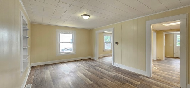 empty room featuring wood-type flooring, crown molding, and wood walls