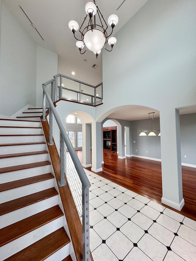 stairway featuring a notable chandelier, wood-type flooring, and a high ceiling