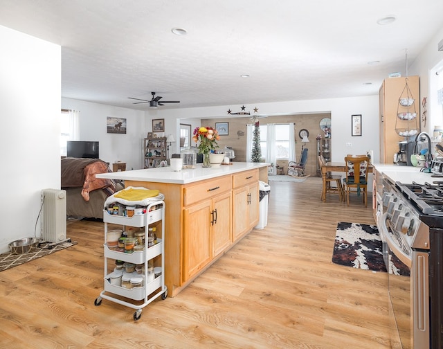 kitchen with light brown cabinetry, stainless steel range oven, light hardwood / wood-style flooring, radiator heating unit, and ceiling fan