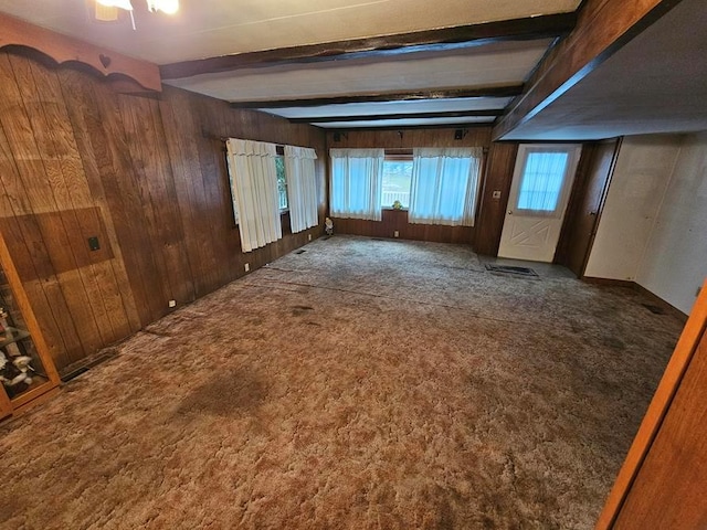 empty room with beamed ceiling, dark carpet, and wooden walls