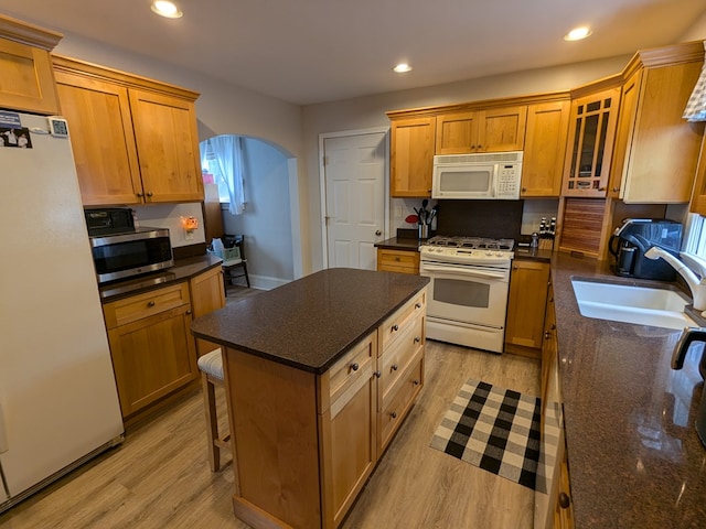 kitchen with white appliances, sink, light hardwood / wood-style floors, a kitchen island, and a breakfast bar area