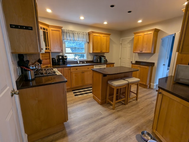 kitchen featuring a center island, sink, dark stone countertops, light hardwood / wood-style floors, and a breakfast bar area