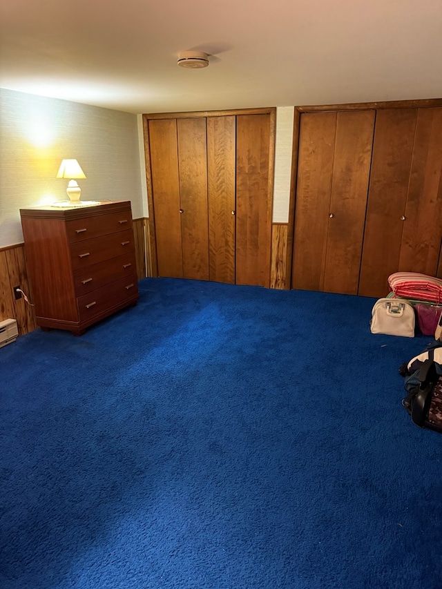 unfurnished bedroom with carpet flooring, multiple closets, and wood walls