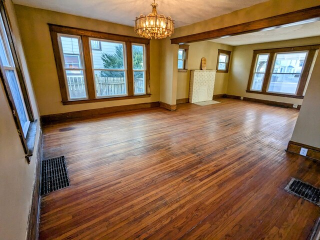 unfurnished living room featuring a notable chandelier, dark hardwood / wood-style floors, and a healthy amount of sunlight