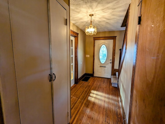 doorway with dark wood-type flooring, a chandelier, and a textured ceiling