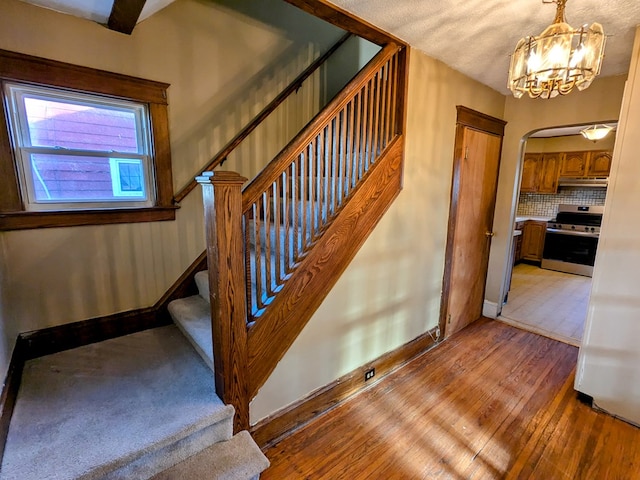 staircase with hardwood / wood-style floors and a chandelier