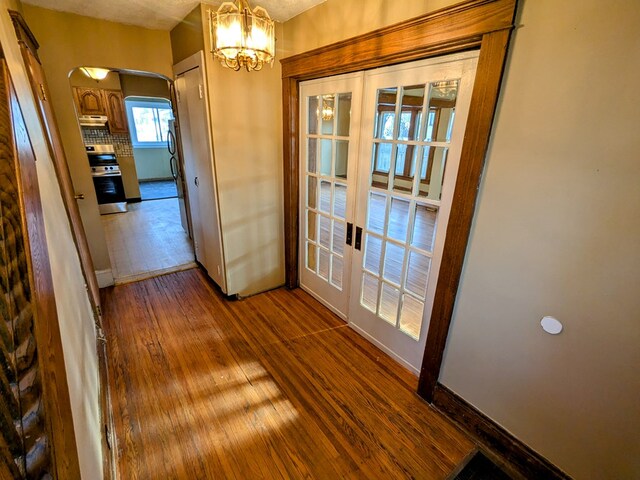 unfurnished dining area featuring wood-type flooring, a notable chandelier, and french doors