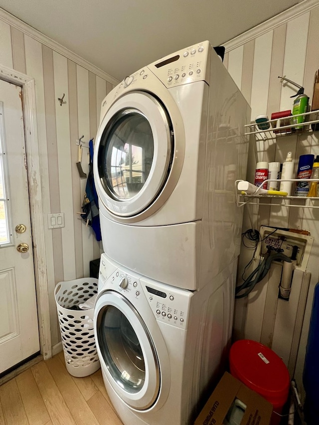 laundry room featuring stacked washer and dryer, crown molding, and light hardwood / wood-style floors