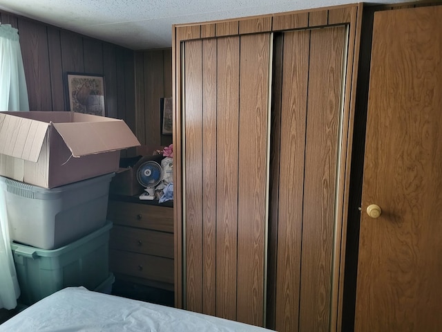 bedroom featuring a textured ceiling, wooden walls, and a closet