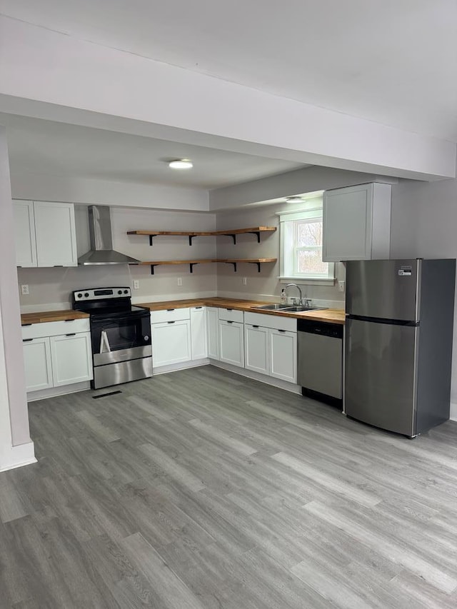 kitchen featuring sink, light hardwood / wood-style flooring, appliances with stainless steel finishes, white cabinets, and wall chimney exhaust hood