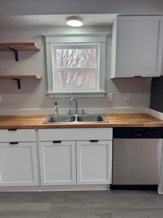 kitchen with sink, butcher block countertops, white cabinetry, stainless steel dishwasher, and hardwood / wood-style floors