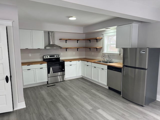 kitchen featuring appliances with stainless steel finishes, wood counters, sink, white cabinets, and wall chimney range hood