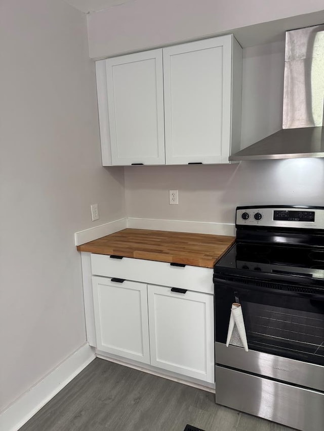 kitchen featuring wall chimney exhaust hood, butcher block countertops, stainless steel range with electric stovetop, dark hardwood / wood-style floors, and white cabinets