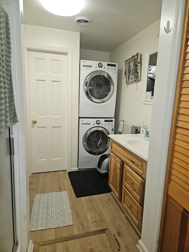 washroom with sink, light hardwood / wood-style floors, and stacked washer and clothes dryer