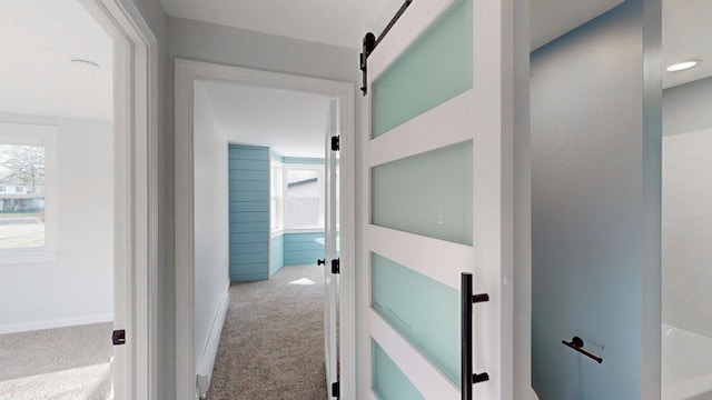 hallway featuring a barn door and light carpet