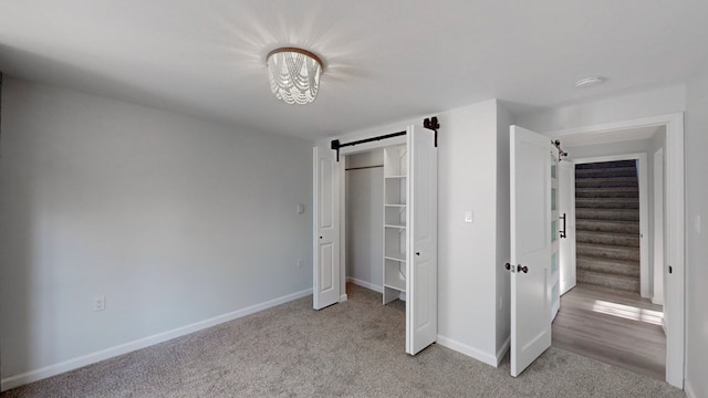 unfurnished bedroom with light carpet, a barn door, and a chandelier