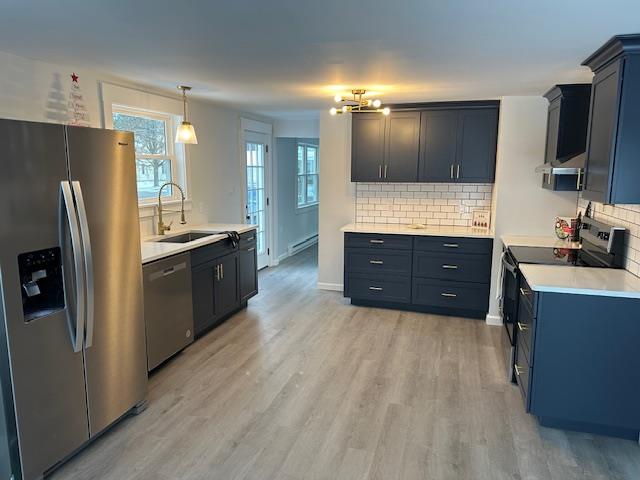 kitchen featuring pendant lighting, sink, light wood-type flooring, tasteful backsplash, and stainless steel appliances