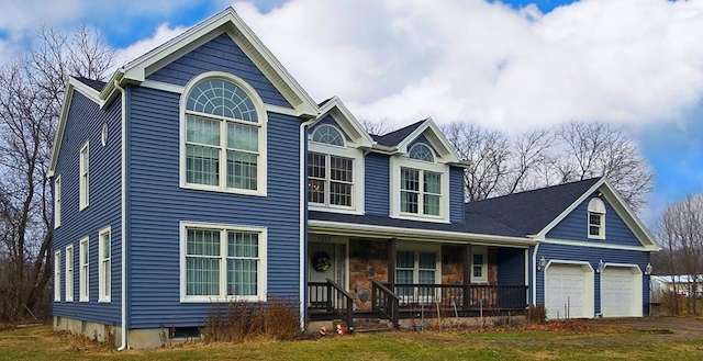 view of property featuring a garage, covered porch, and a front lawn