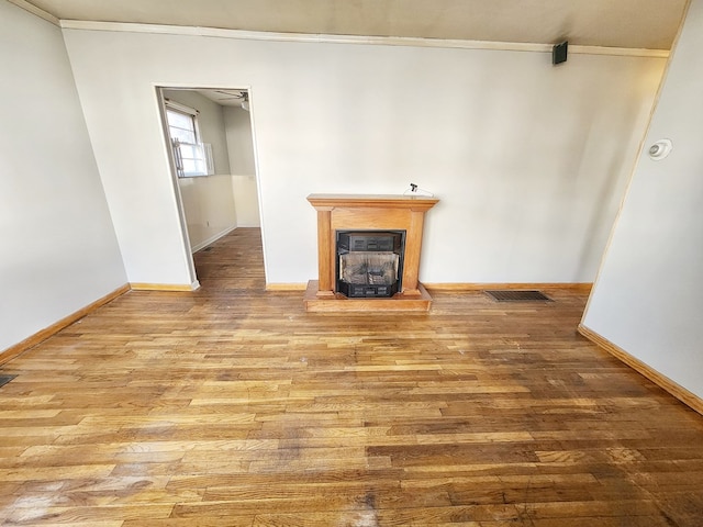 unfurnished living room with light hardwood / wood-style floors, a wood stove, and crown molding