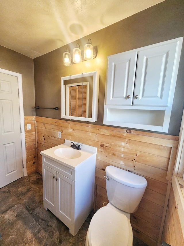 bathroom with wooden walls, vanity, and toilet