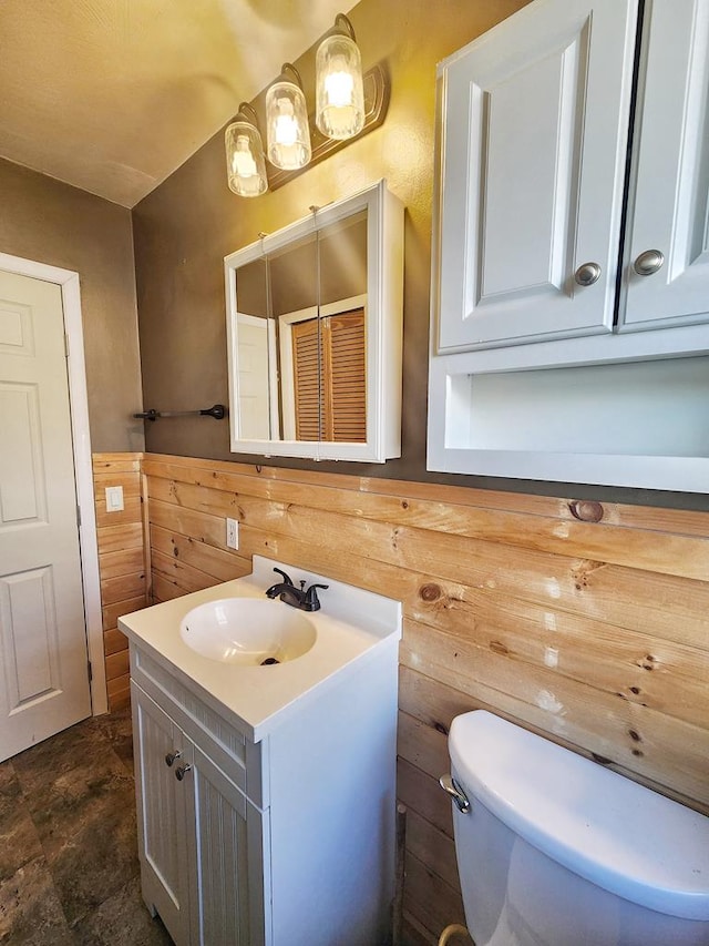 bathroom featuring vanity, toilet, and wood walls